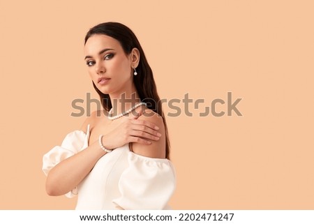 Beautiful young woman with stylish pearl jewelry on beige background Royalty-Free Stock Photo #2202471247
