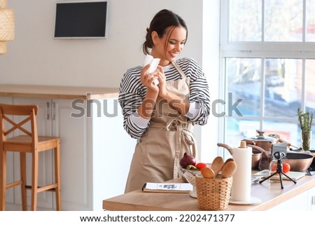 Young woman wiping her hands with paper towel while watching cooking video tutorial in kitchen Royalty-Free Stock Photo #2202471377