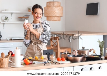 Young woman wiping her hands with paper towel while watching cooking video tutorial in kitchen Royalty-Free Stock Photo #2202471379