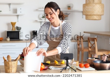 Young woman taking paper towel while following cooking video tutorial in kitchen Royalty-Free Stock Photo #2202471381