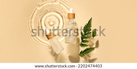 Bottles of cosmetic serum and fern leaves in water on beige background, top view