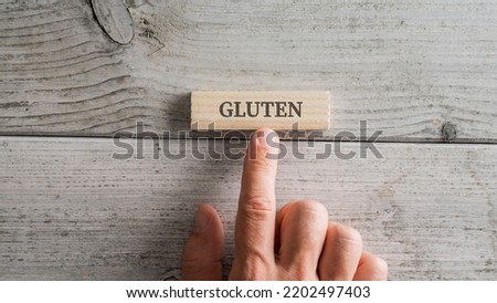 Male hand placing wooden peg with a Gluten sign on it over white textured wooden background.
