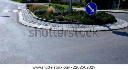 A flower bed at an intersection with curved curbs. Pedestrians pass through to crosswalk. The arrow directs vehicles to the correct lane of the road at the highway exit