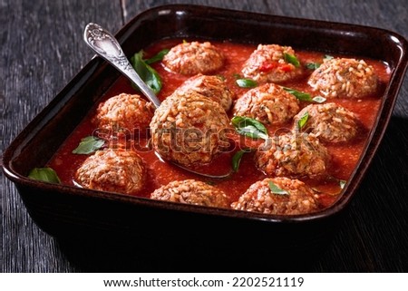 Italian Porcupine Balls, ground beef and rice meatballs in tomato sauce in rustic baking dish on dark wooden table, horizontal view from above, close-up