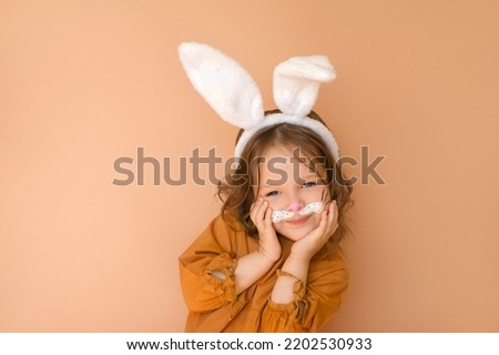 A cute curly-haired girl with white rabbit ears and a painted face looks at the camera. New Year according to the Chinese Eastern calendar.  Waiting for the holidays