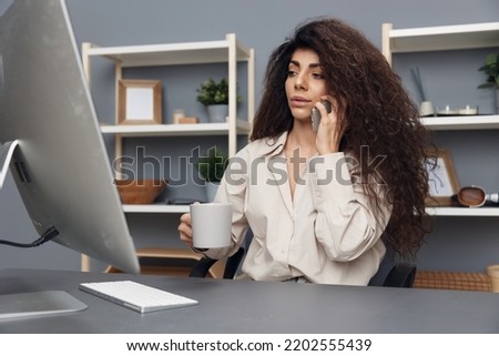 Focused on work tanned adorable curly Latin businesswoman in linen shirt talk using phone in home office. Copy space Mockup Banner. Attractive freelancer work from home using modern desktop computer