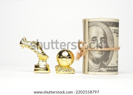 A picture of miniature golden ball and and boots trophy with fake money on white background