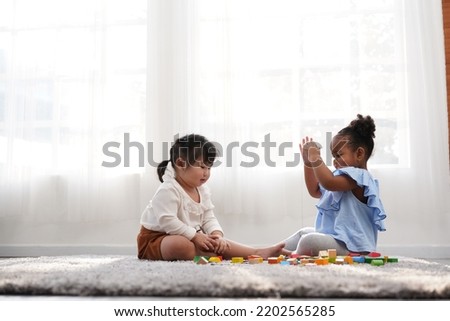 Two female kid playing in the home school with wooden block as creative learning. African girl and Asain girl are playing together with fun. Royalty-Free Stock Photo #2202565285