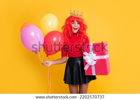 surprised kid in crown with present box and party balloon on yellow background