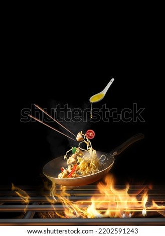 Flying Spaghetti with chicken and vegetables in a pan on fire - black background-Copy space Royalty-Free Stock Photo #2202591243