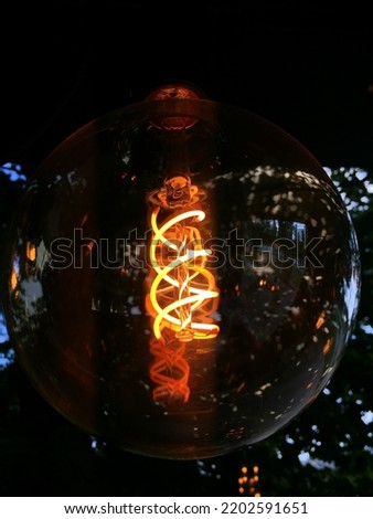 Beautiful filament in a large bright yellow-orange bulb inside a glass shell. In the background, a city street is visible through the glass. Royalty-Free Stock Photo #2202591651