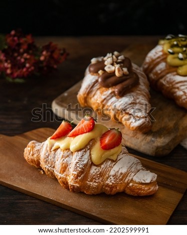 Freshly baked croissant, with strawberries and cream on top. Dark wooden background