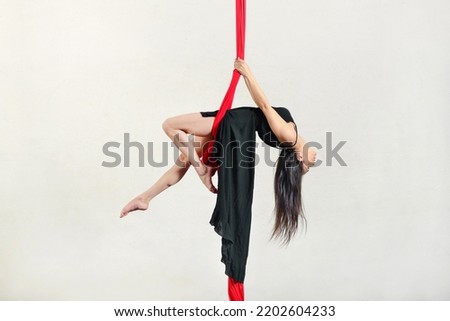 Full body side view of active female aerialist performing swing exercise on aerial silks against white background during training in studio