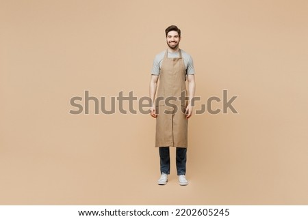 Full body smiling fun young man barista barman employee wear brown apron work in coffee shop look camera isolated on plain pastel light beige background studio portrait Small business startup concept Royalty-Free Stock Photo #2202605245