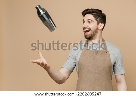 Young excited happy man barista barman employee in brown apron work in bar pub club toss up shaker make alcohol cocktail isolated on plain pastel light beige background Small business startup concept Royalty-Free Stock Photo #2202605247