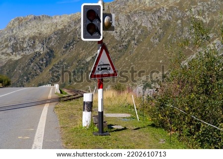 Crossing of railway track and mountain pass road with warning light at Swiss mountain pass Furkapass on a sunny late summer day. Photo taken September 12th, 2022, Furka Pass, Switzerland.