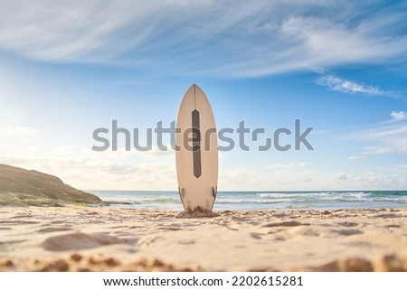 Surfboard for surfing staying on beach sand. Ocean waves at the background. Longboard or sup for water sport by sea water. Summer vacations, sport on shore vibes concept
