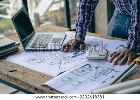 engineer working in office draw a construction project An architect's hand-drawn print engineer discusses floor plans over architectural blueprints at a desk in a modern office.