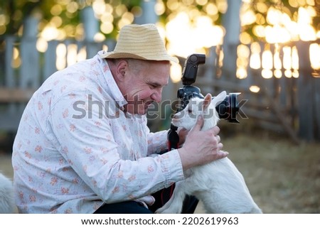 A photographer takes a picture of an animal. A man with a camera wants to take a picture of a funny little goat.