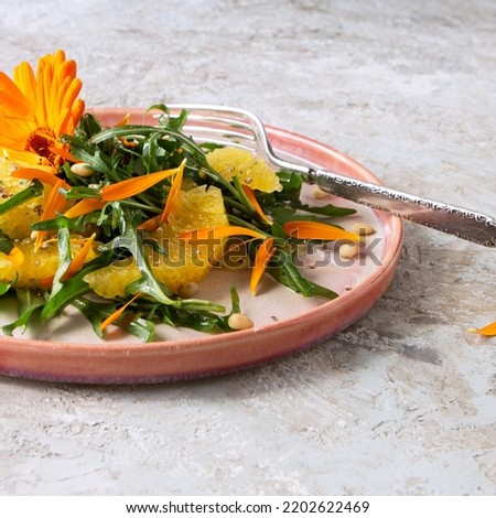 plate with salad with arugula, oranges and edible marigold flowers on the table