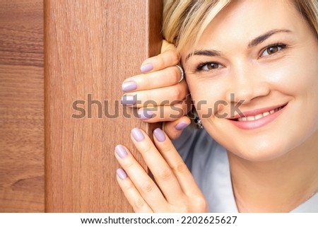 Close up portrait of the young smiling caucasian woman looks out from behind the door looking at the camera