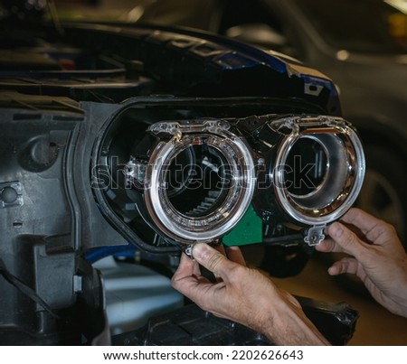 Car headlight in repair close-up. The car mechanic installs the lens in the headlight housing. The concept of a car service.Installation of LED lenses in the headlight. LED lens.Restoration of optics. Royalty-Free Stock Photo #2202626643