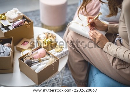 Closeup female hands writing Christmas festive congratulations on card for gift box package use elegant golden pen. Woman handwrite postage congrats preparation New Year presents for friends relatives