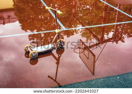 Reflection of children's scooter and basketball hoop in the puddle at playground. rainy weather