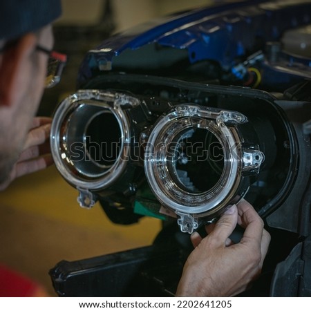 Car headlight in repair close-up. The car mechanic installs the lens in the headlight housing. The concept of a car service.Installation of LED lenses in the headlight. LED lens.Restoration of optics. Royalty-Free Stock Photo #2202641205