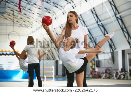 Sport training with coach. Preparing for sport competition. Beginner gymnastics athletes doing exercises with gymnastics equipment at sports gym, indoors. Concept of achievements, studying, goals Royalty-Free Stock Photo #2202642175