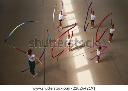 Ribbon exercises. Aerial view. Female sports coach training gymnastics athletes at sports gym, indoors. Concept of achievements, studying, goals. Coaching, training, child psychology