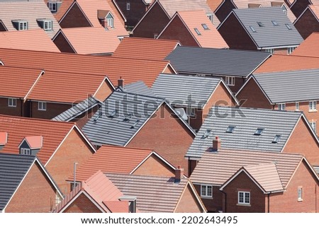 An aerial photograph taken from a helicopter of the roofs of a new build housing estate in the UK. An abstract view of red and grey tiled roofs in a large housing development. Royalty-Free Stock Photo #2202643495