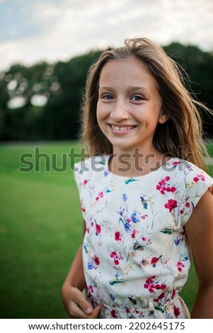 Outdoor portrait of smiling little girl with long blonde hair in summer park.