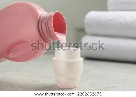 Pouring laundry detergent from bottle into cap on light grey marble table, closeup