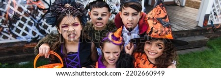 Interracial preteen friends in halloween costumes grimacing at camera outdoors, banner