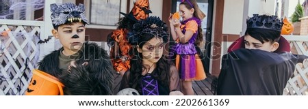 Asian boy in costume looking at friends with bucket during halloween celebration outdoors, banner