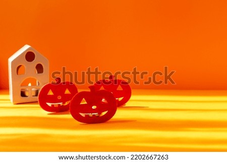 Halloween. Artificial pumpkins and a house with a burning candle stand on an orange background in the sunlight