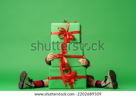 cute little girl of 7 years old with curly hair in golden deer horns, sitting with gift boxes on a green background in studio. child smiles happily and looks into the frame. Advertising. copy space