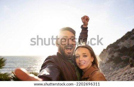 Beautiful young couple having fun taking a selfie portrait against a beautiful panorama at sunset. Boyfriend and girlfriend in love smiling at the camera together. People and lifestyle concept.
