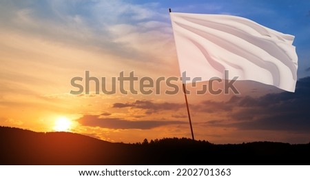 White flag waving in the wind on flagpole against the sunset sky with clouds. White flag is a symbol of surrender.