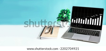 Laptop screen shows a graph of the 2023 economy rising and is placed on wooden desk in office. Business growth concept. technology work notebook computer network copy space, close-up, blue background