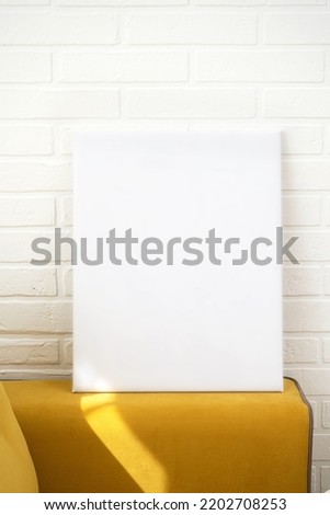Mock up poster. Poster layout. Blank white canvas, gray brick wall and yellow sofa back.