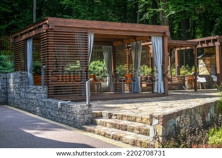 Close up wooden gazebo decorated with gabion elements and natural stone pavement. 