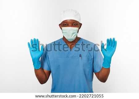 Black surgeon doctor man in blue coat white cap surgeon mask and sterile blue gloves isolated on white background. Adult black african american practicing surgeon portrait aseptic blue gloves Royalty-Free Stock Photo #2202721055