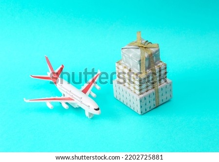 Stack of Christmas gift boxes wrapped in bow with air plane model on a turquoise background. Holiday delivery. Merry Christmas, travel concept