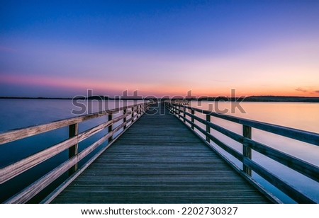 Wooden lake pier at dawn. Lake pier at dawn. Beautiful sunrise over lake pier. Lake pier at dawn landscape Royalty-Free Stock Photo #2202730327