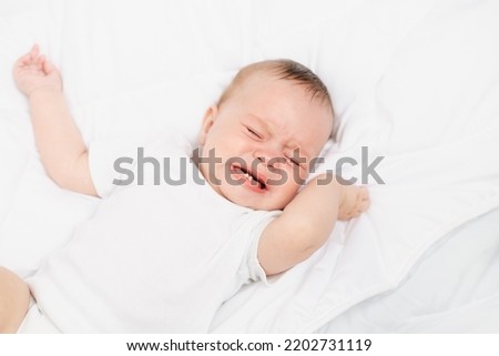 The baby is crying in his crib . The baby 's teeth are teething . Colic in babies . Hungry baby . Baby on a white background Royalty-Free Stock Photo #2202731119