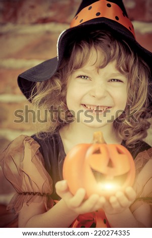 Funny child dressed witch costume holding pumpkin. Halloween holidays concept
