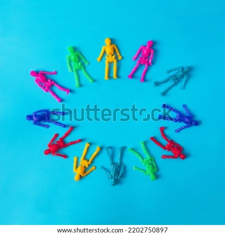 Mini skeletons in different colors making an ellipse on blue background.  Surreal spooky creative concept for Halloween celebration banner or party invitation Royalty-Free Stock Photo #2202750897