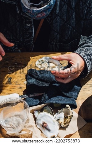 woman shucking and eating oysters at outdoor restaurant  Royalty-Free Stock Photo #2202753873